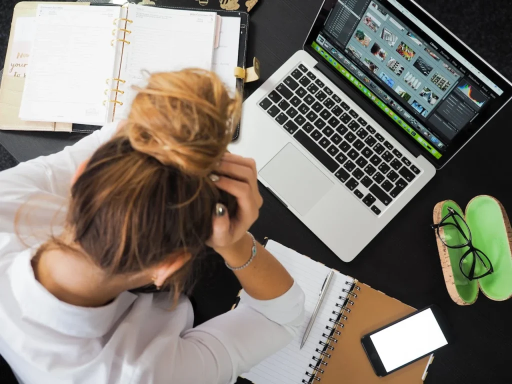 Frustrated person at a desk with a laptop, phone and notebook